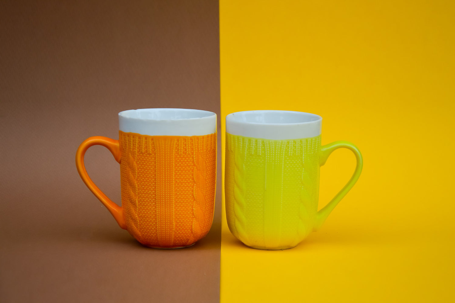 Ceramic mugs with intricate knitted patterns in shades of orange and yellow against a warm brownyellow backdrop.