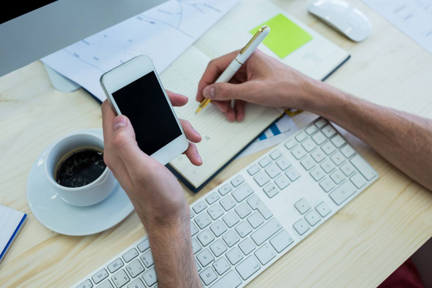 Male graphic designer jotting down ideas in a diary while holding a mobile phone.