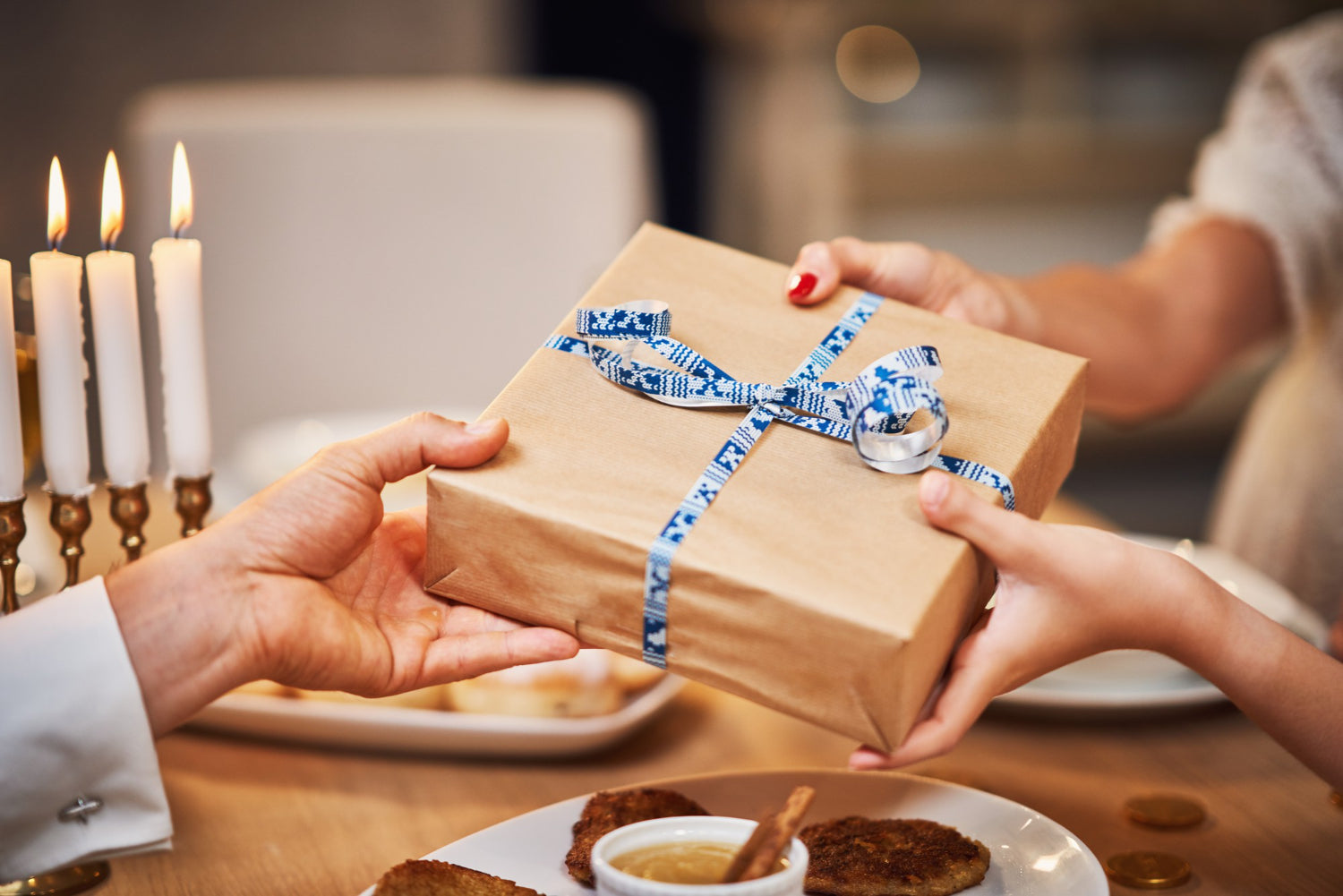 Gift giving with a family gathered around the table for a Hanukkah dinner with traditional dishes.