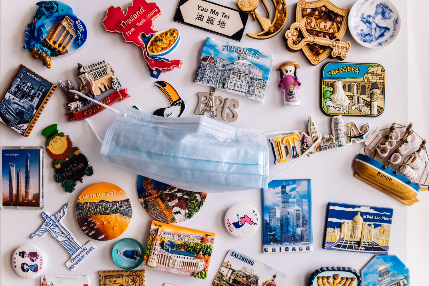 Collection of refrigerator magnets displaying various countries' landmarks, each adorned with a face protection mask.