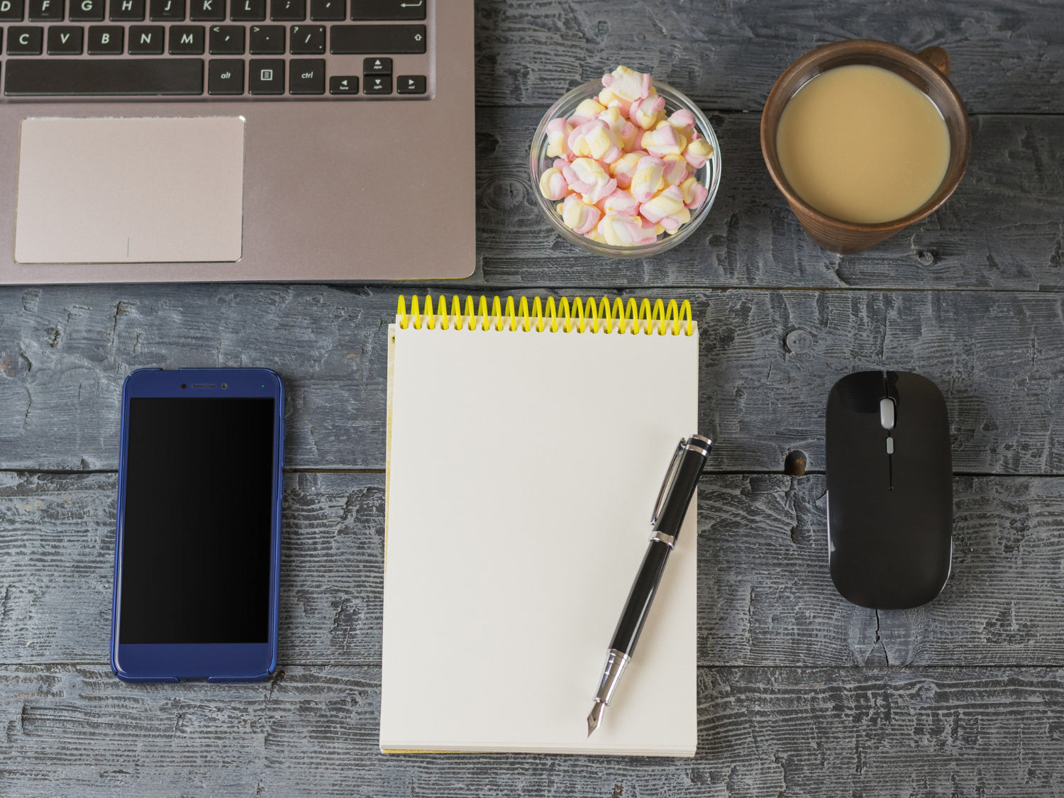 An opened notebook laptop, a sleek fountain pen, and a computer mouse placed on a dark wooden table.